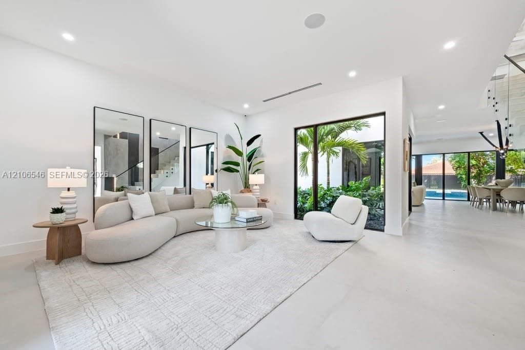 Living area featuring large-format tile flooring, floor-to-ceiling mirrors, recessed lighting, and expansive glass walls opening to an interior garden