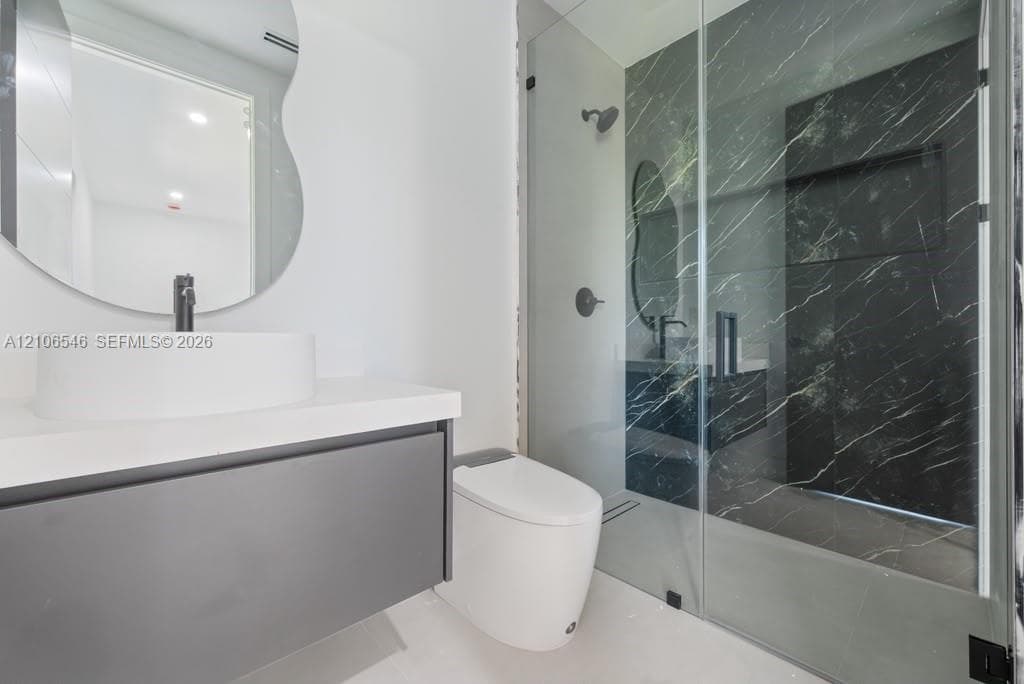 Floating vanity with a white vessel sink, dark stone-finish shower surround, glass shower enclosure, and organic-shaped wall mirror