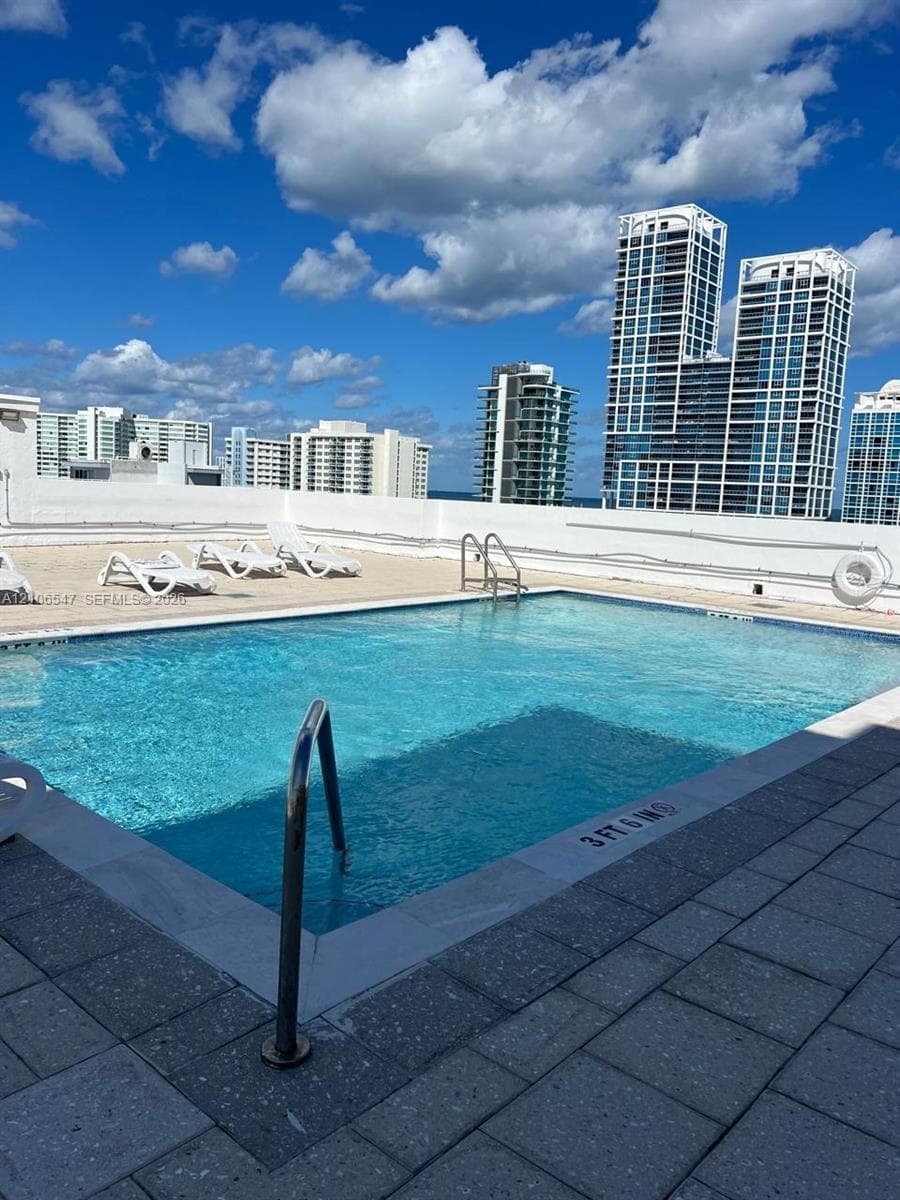 Rooftop swimming pool with stainless steel handrails, expansive stone-paver decking, and perimeter wall safety railing