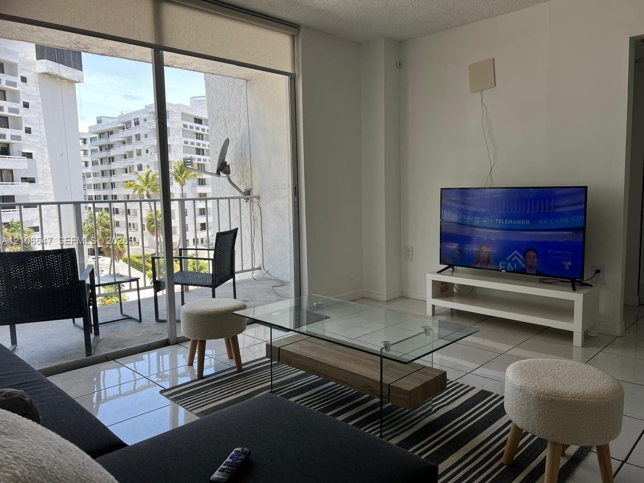 Floor-to-ceiling sliding glass doors, white tiled flooring, and a private balcony with metal railing