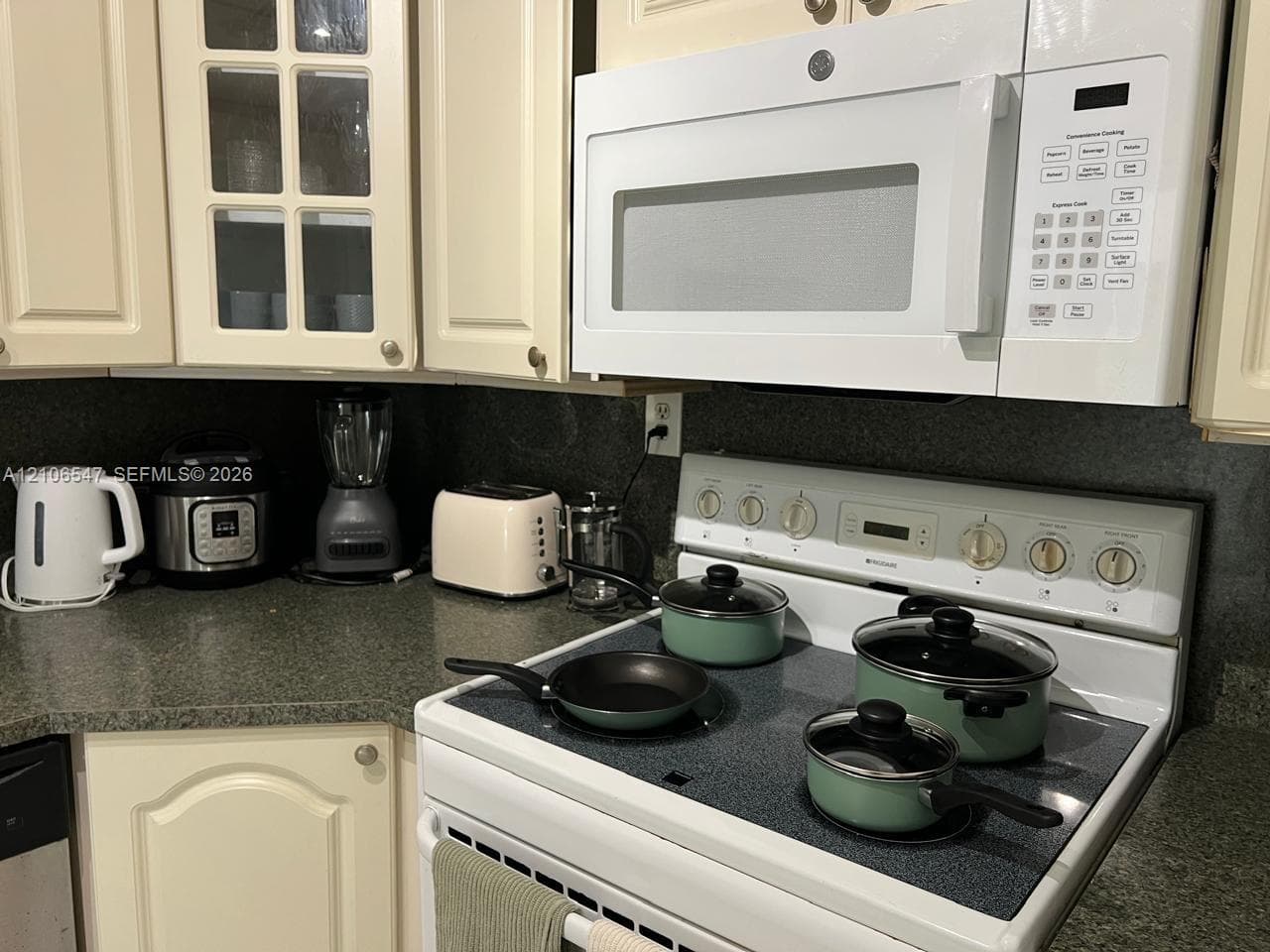 Kitchen featuring off-white raised-panel cabinetry, glass-front cabinet accents, solid-surface countertops, and a white over-the-range microwave