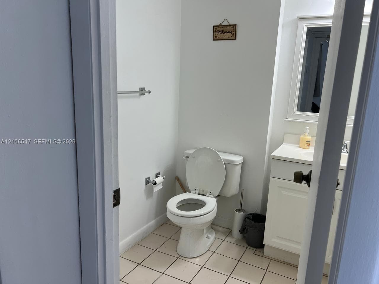 Bathroom featuring a white vanity cabinet with a integrated countertop, framed wall mirror, tiled flooring, and polished chrome hardware