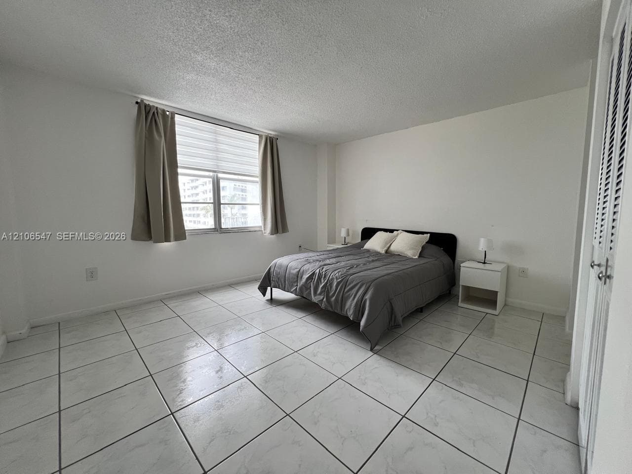 Large-format neutral tile flooring, multi-pane window, and louvered closet doors