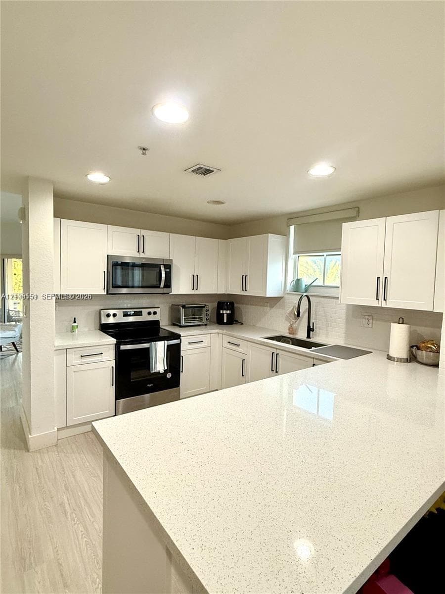 Kitchen featuring white shaker-style cabinetry, solid-surface countertops, recessed lighting, and stainless steel appliances