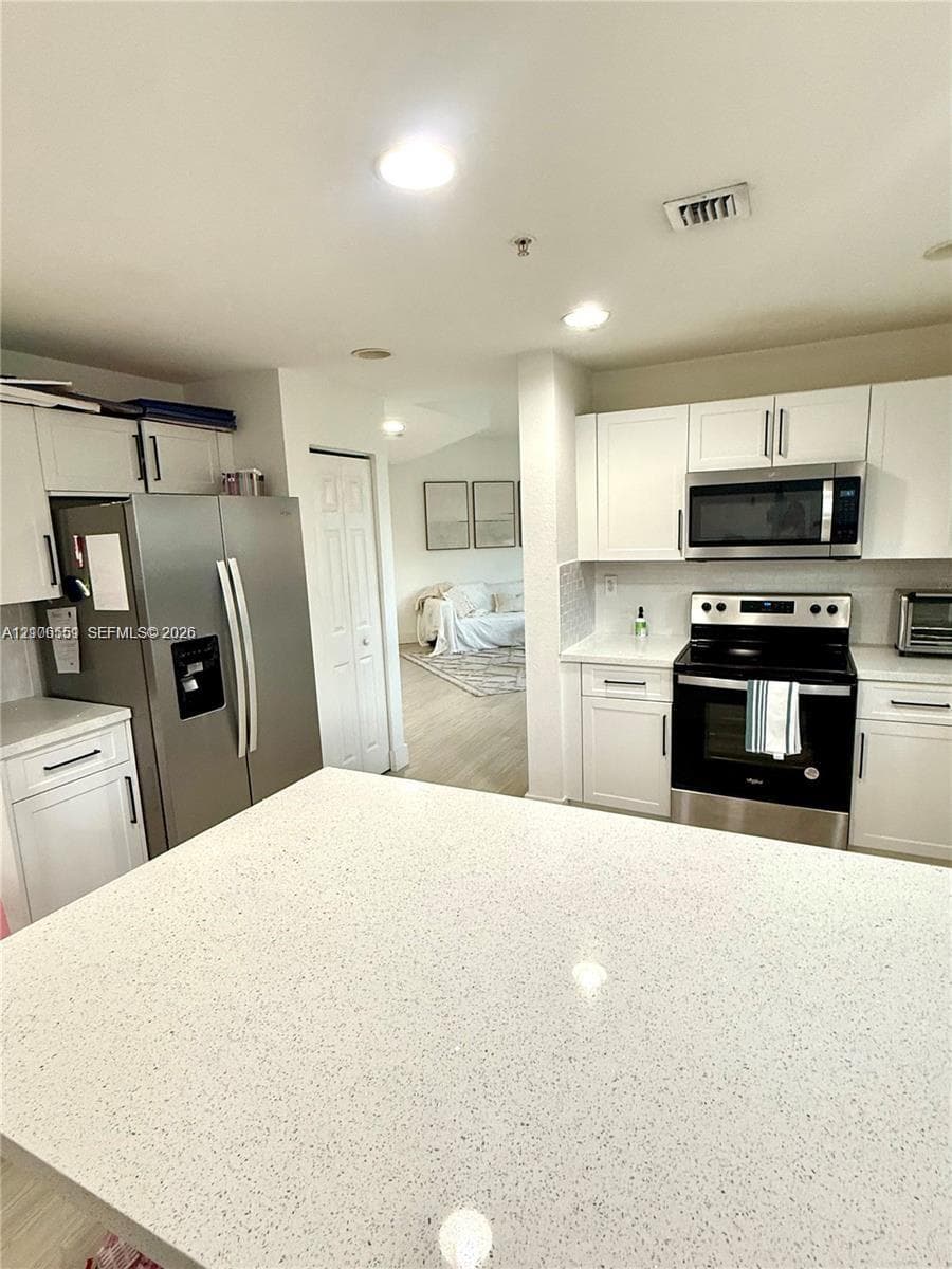Kitchen featuring white cabinetry, solid surface quartz-style countertops, stainless steel appliances, and recessed ceiling lighting