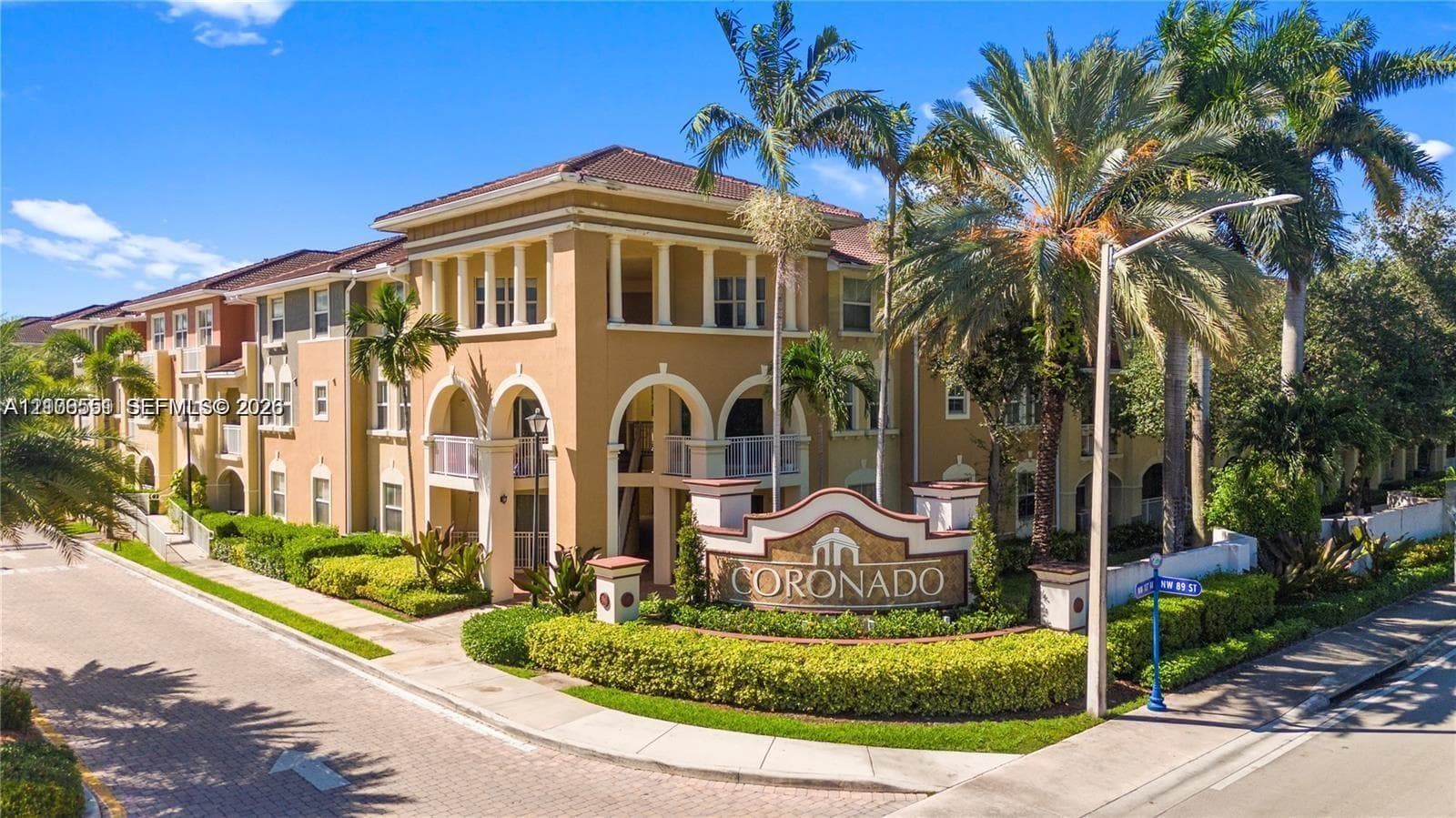 Mediterranean-style building featuring stucco exterior walls, arched architectural detailing, multi-level private balconies, and landscaped grounds with mature palm trees