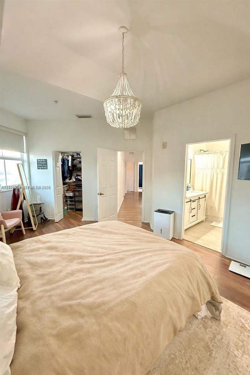 Vaulted ceiling featuring a central beaded chandelier, wood-finish flooring, and double-door entry to a walk-in closet