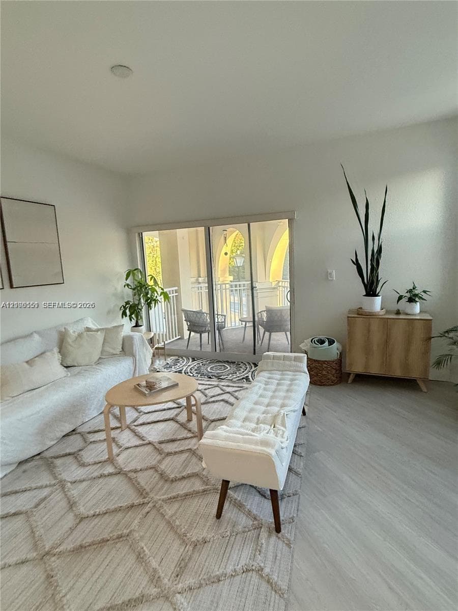 Living area featuring light-toned wood-finish flooring and sliding glass doors opening to a covered balcony