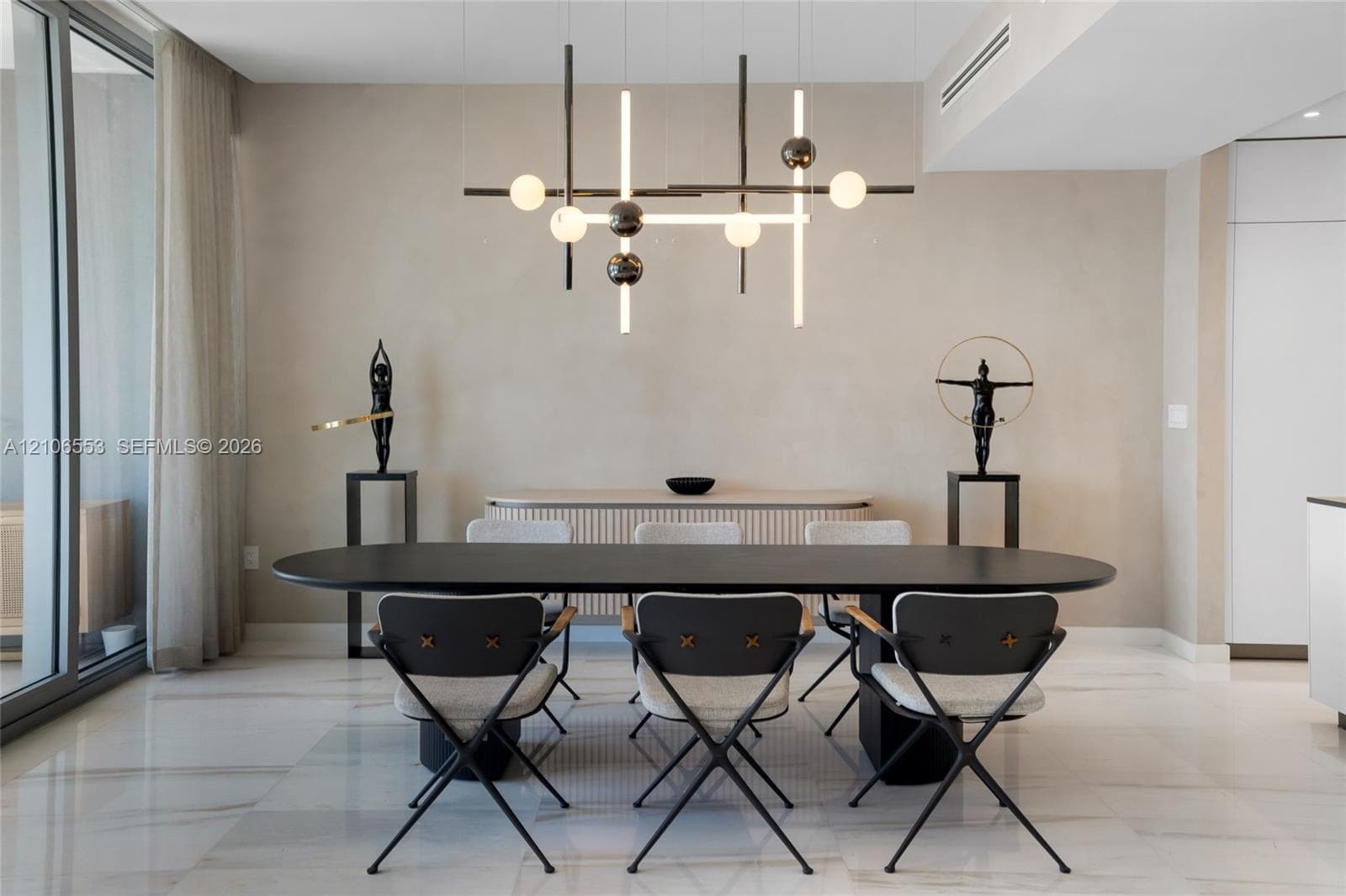 Modern living space featuring large-format stone flooring, floor-to-ceiling glass sliding doors, textured wall finishes, and a linear geometric multi-light chandelier
