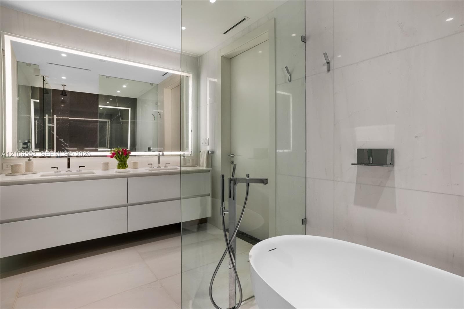 Floating vanity with dual rectangular sinks, oversized backlit mirror, floor-to-ceiling stone wall tiling, glass-enclosed shower, and freestanding soaking tub with floor-mounted faucet