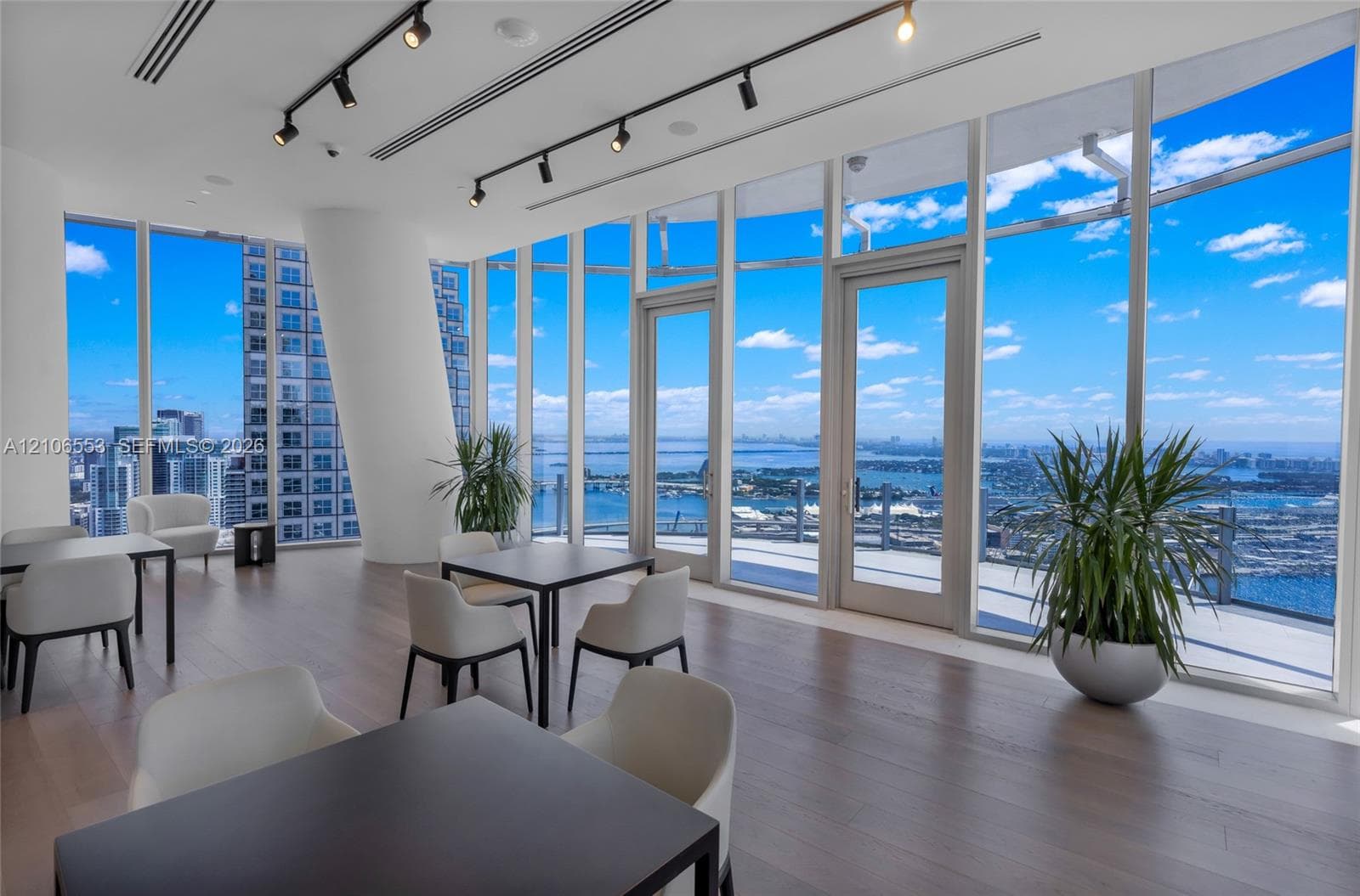 Floor-to-ceiling glass windows, wide-plank wood-finish flooring, linear track lighting, and double glass-paneled doors opening to an exterior terrace