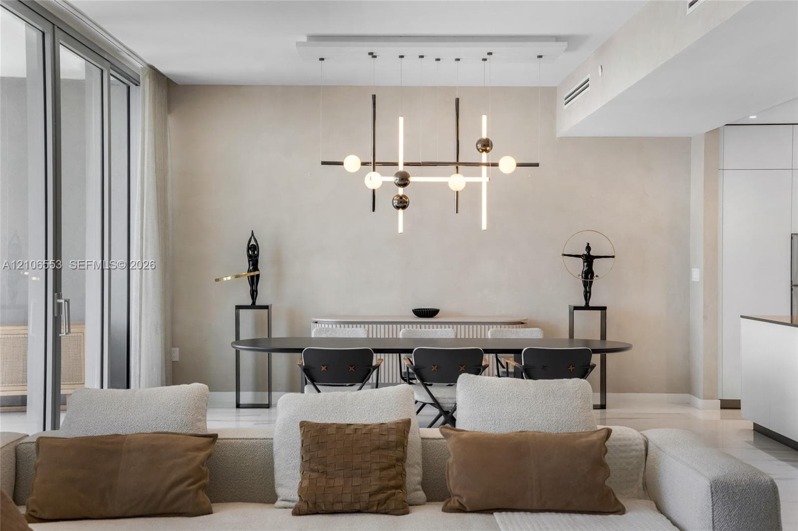 Modern chandelier with structural metallic frame and spherical lighting elements, floor-to-ceiling glass panel door, light-toned wall finishes, and polished flooring