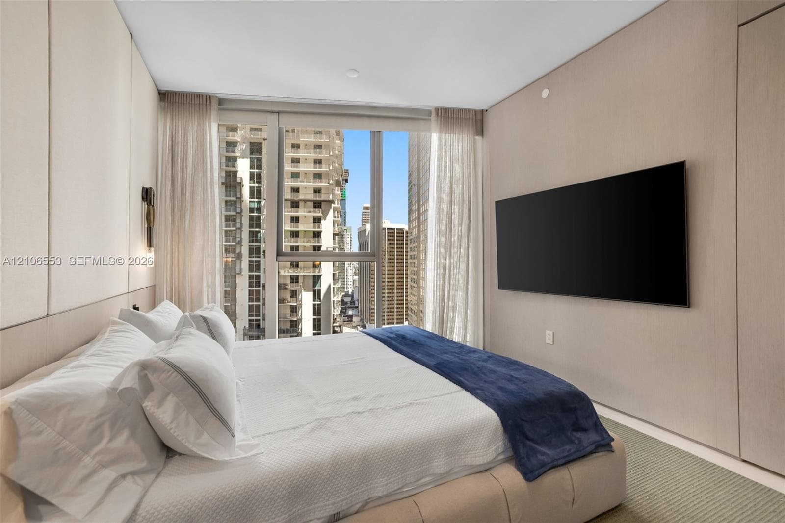 Floor-to-ceiling windows featuring urban scenery, custom wood-paneled wall treatment, integrated wall-mounted lighting, and neutral carpeting