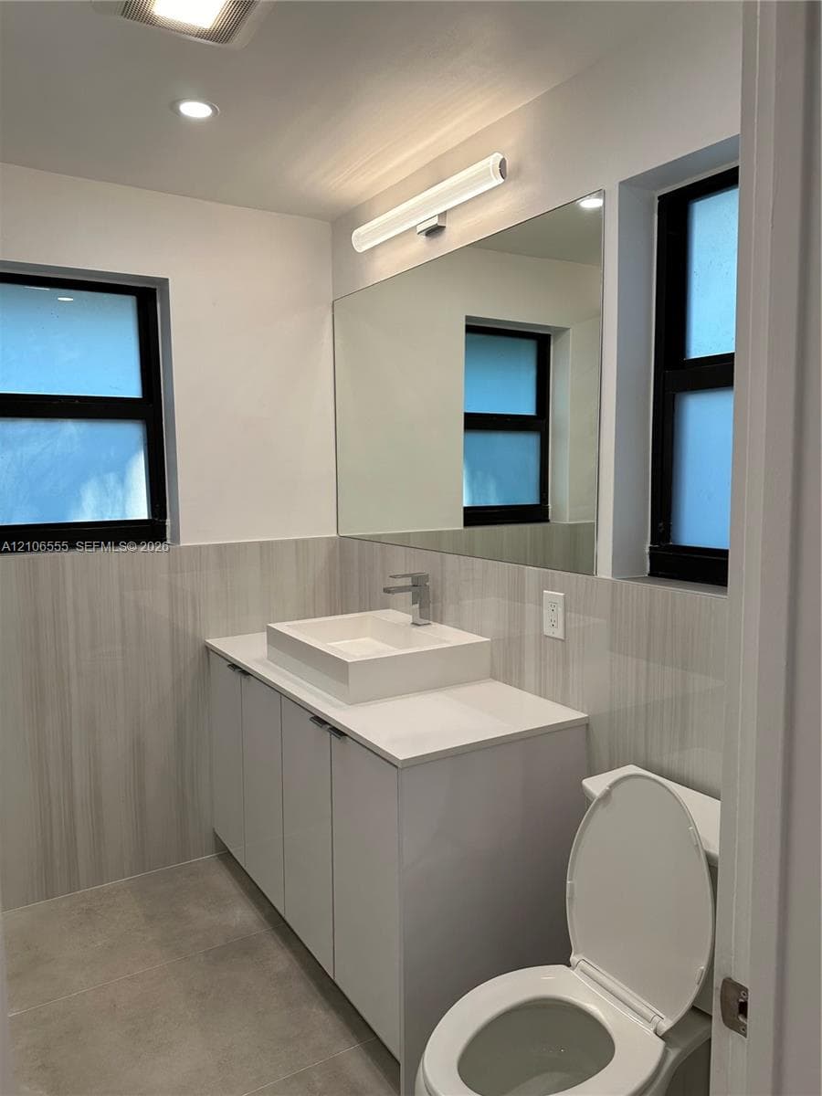 Modern vanity with a rectangular vessel sink, polished countertop, full-width mirror, and neutral wall tile surfacing