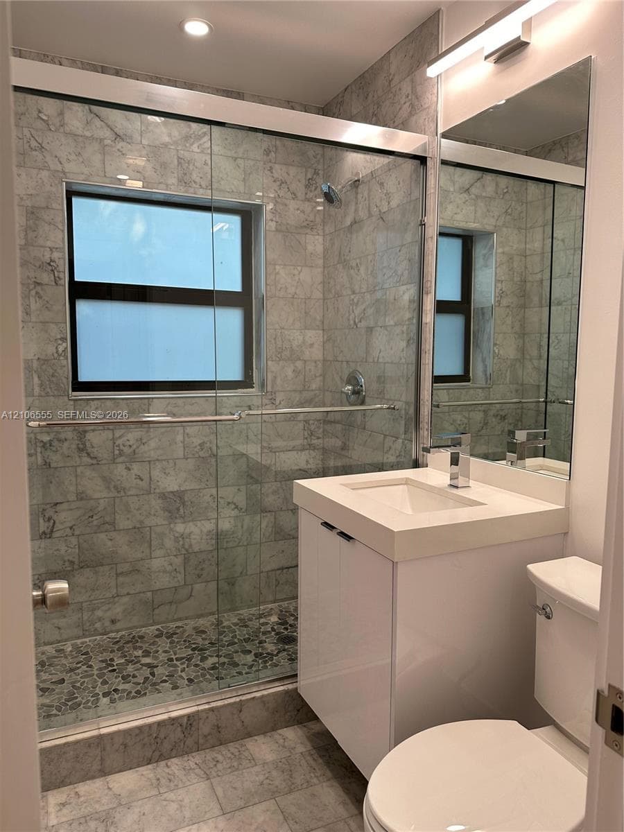 Walk-in shower featuring stone-tiled walls, a natural stone pebble floor, and a frameless glass enclosure, paired with a modern vanity featuring a solid surface countertop and rectangular undermount sink