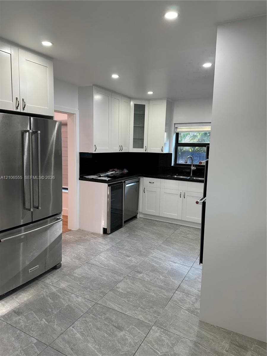 Kitchen featuring shaker-style white cabinetry, contrasting dark countertops, stainless steel appliances, integrated wine refrigerator, and stone-finish tile flooring