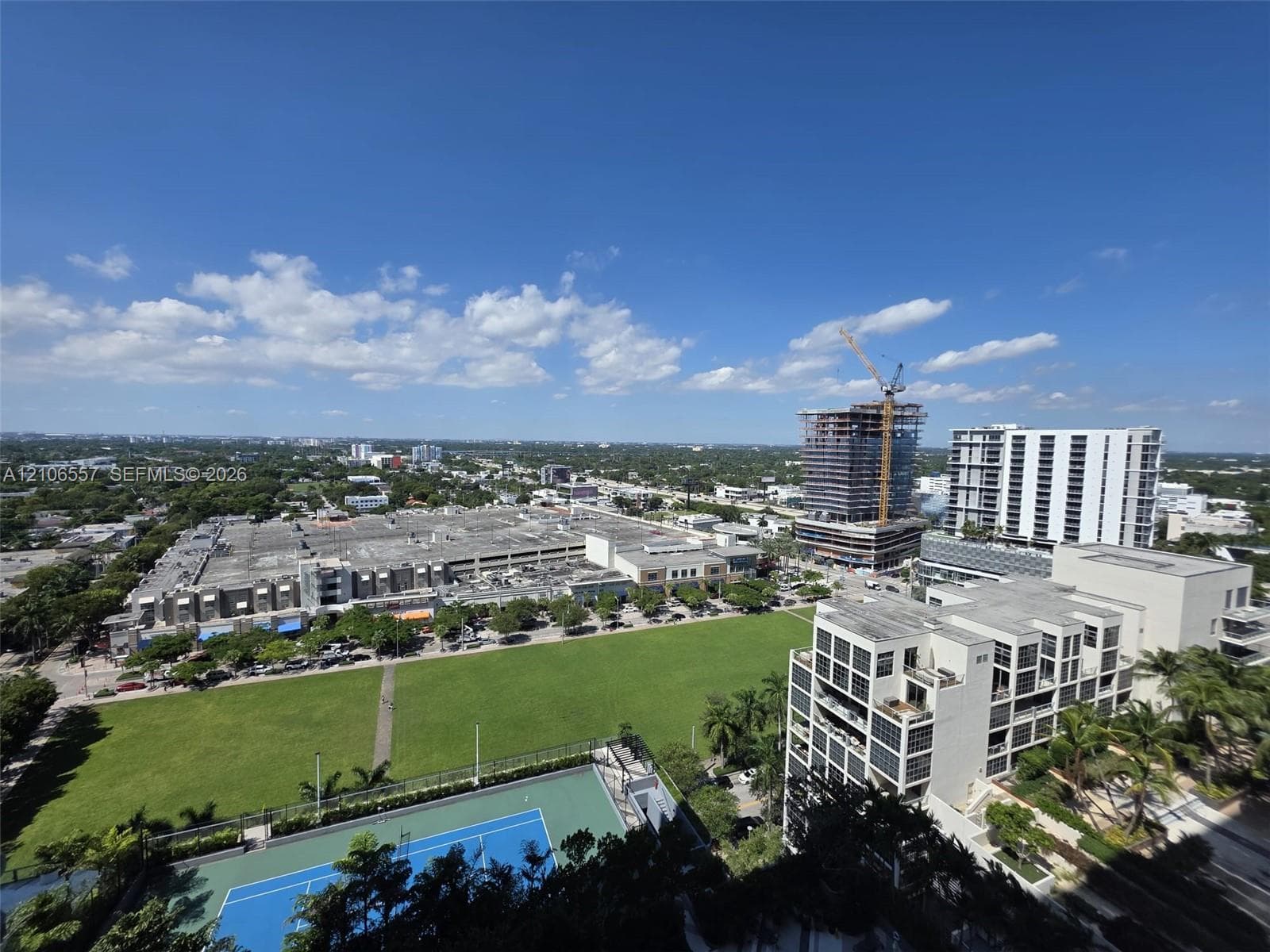 Elevated urban perspective featuring an expansive lawn area and a fenced hard-court tennis facility