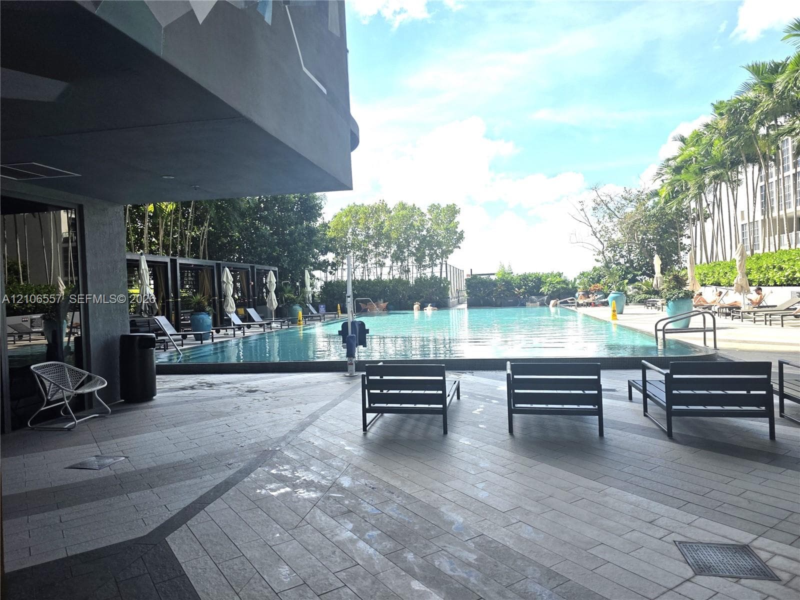Swimming pool featuring a paved deck, built-in structural cabanas, and mature palm tree landscaping