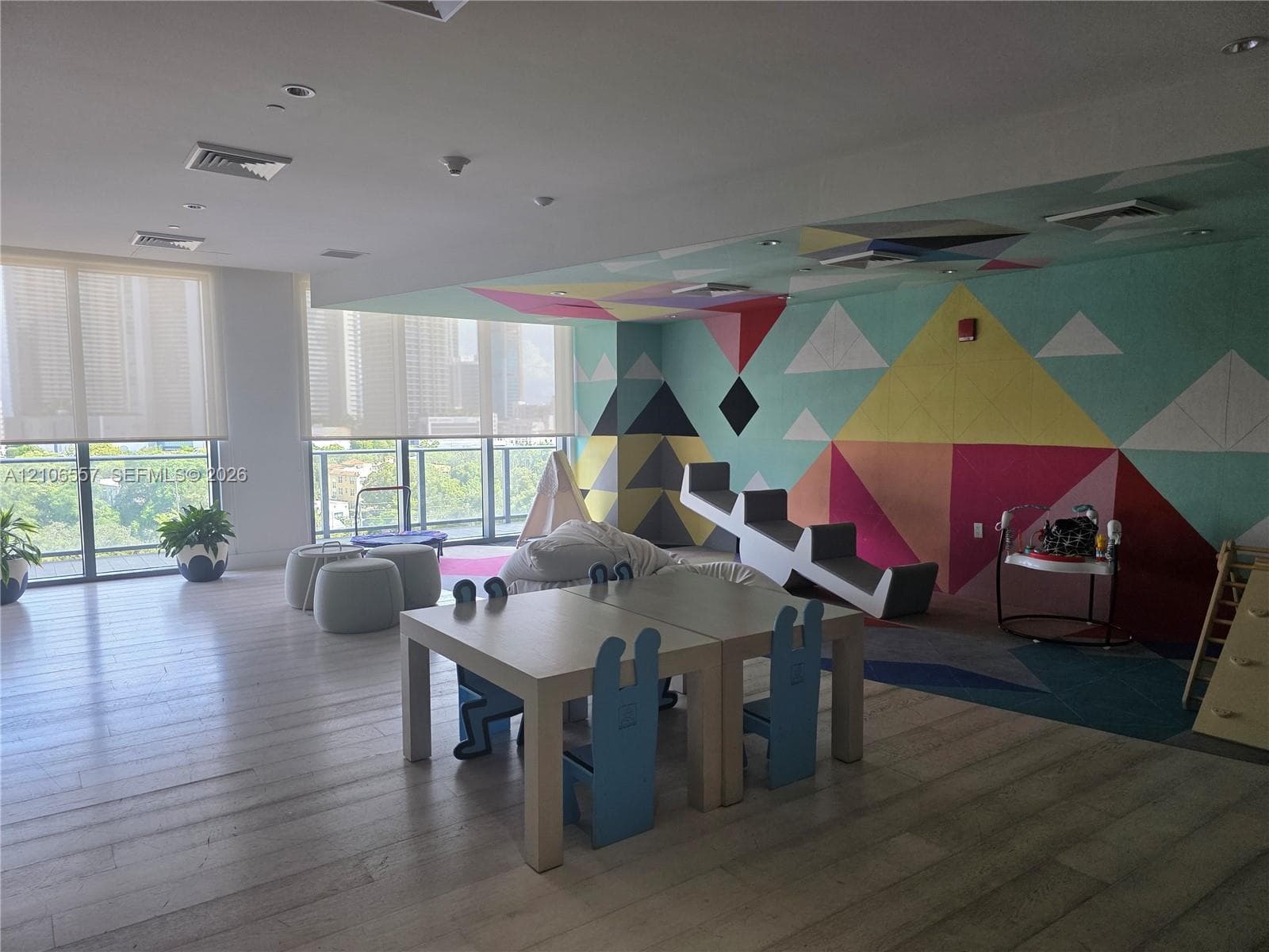 Expansive interior space featuring wood-finish flooring, floor-to-ceiling windows with roller shades, and a geometric-patterned accent wall