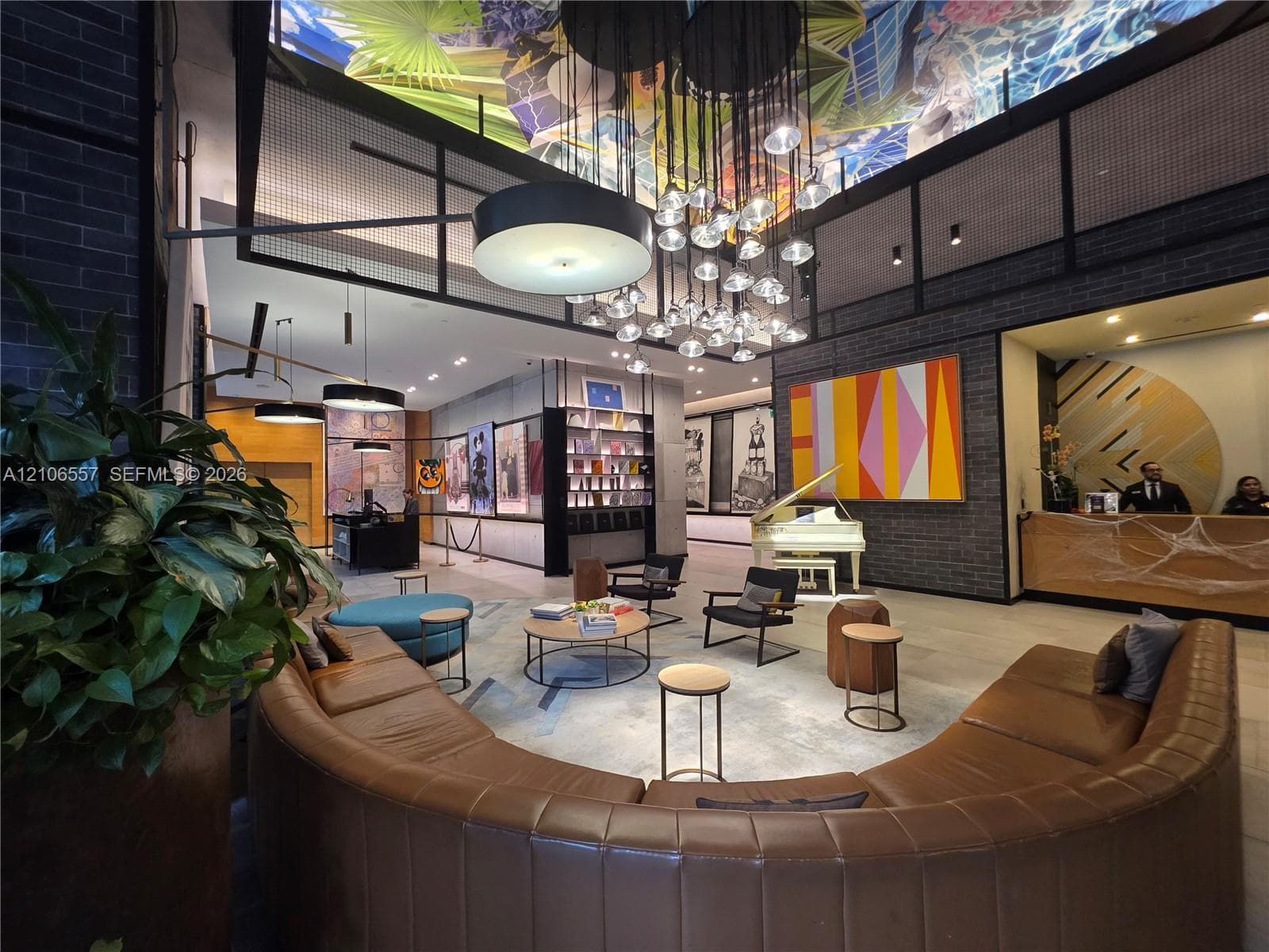Common area featuring a muraled ceiling, multi-pendant cluster chandelier, dark brick masonry walls, and large-format tile flooring
