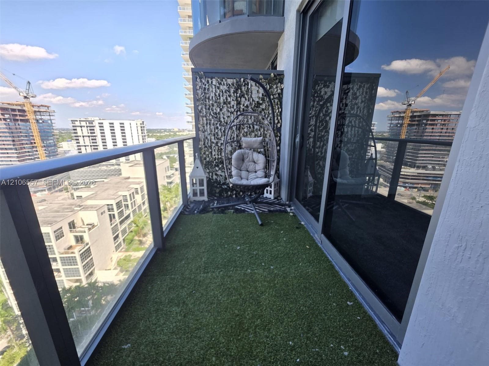 Private balcony featuring glass panel railings, synthetic turf flooring, and large sliding glass door access
