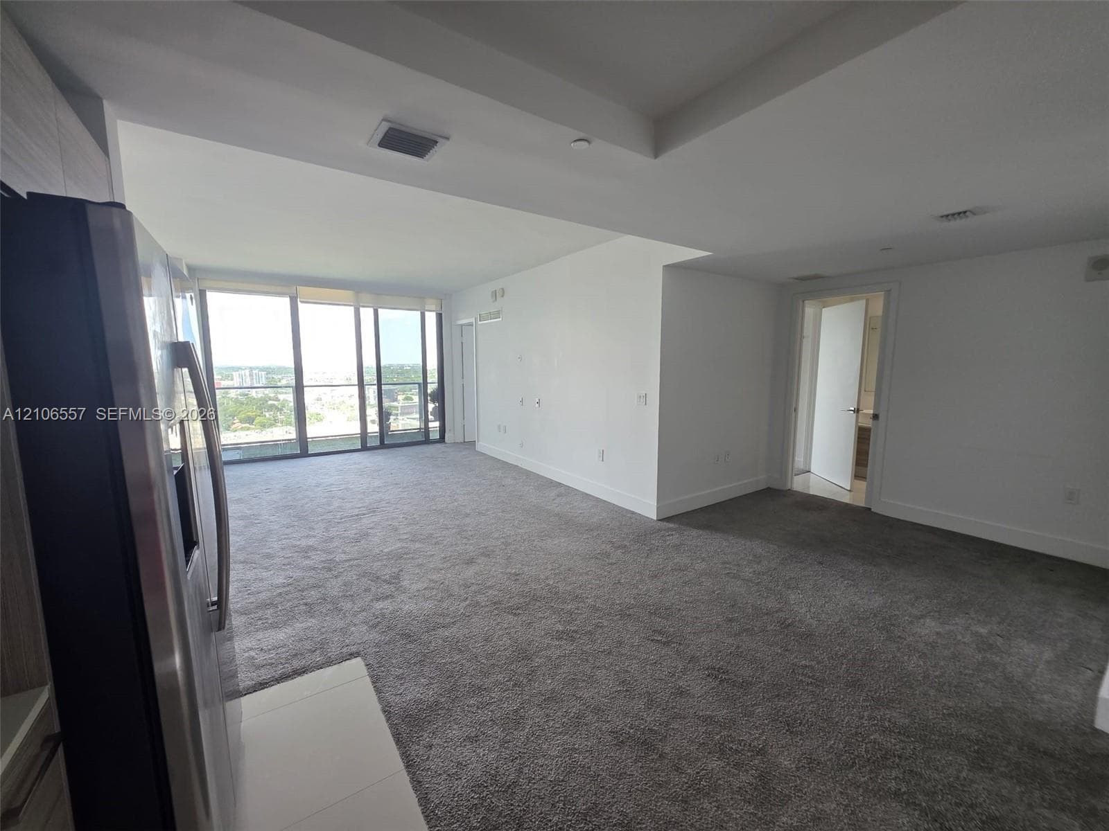Open-concept interior featuring floor-to-ceiling windows, neutral carpeting, a tray ceiling, and a stainless steel refrigerator
