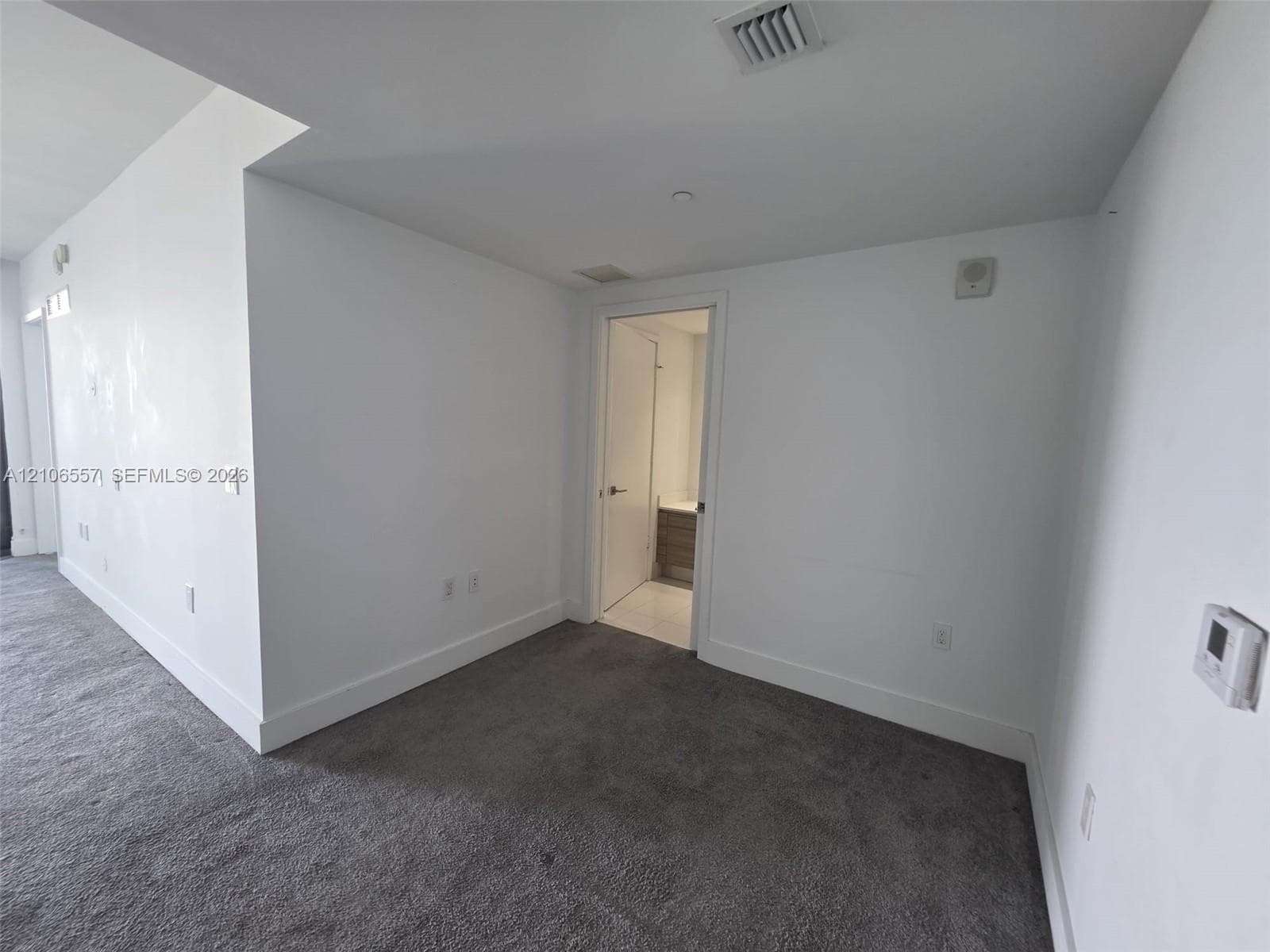 Interior space featuring wall-to-wall carpeting, smooth white walls, recessed ceiling lighting, and a doorway revealing a vanity with wood-finish cabinetry
