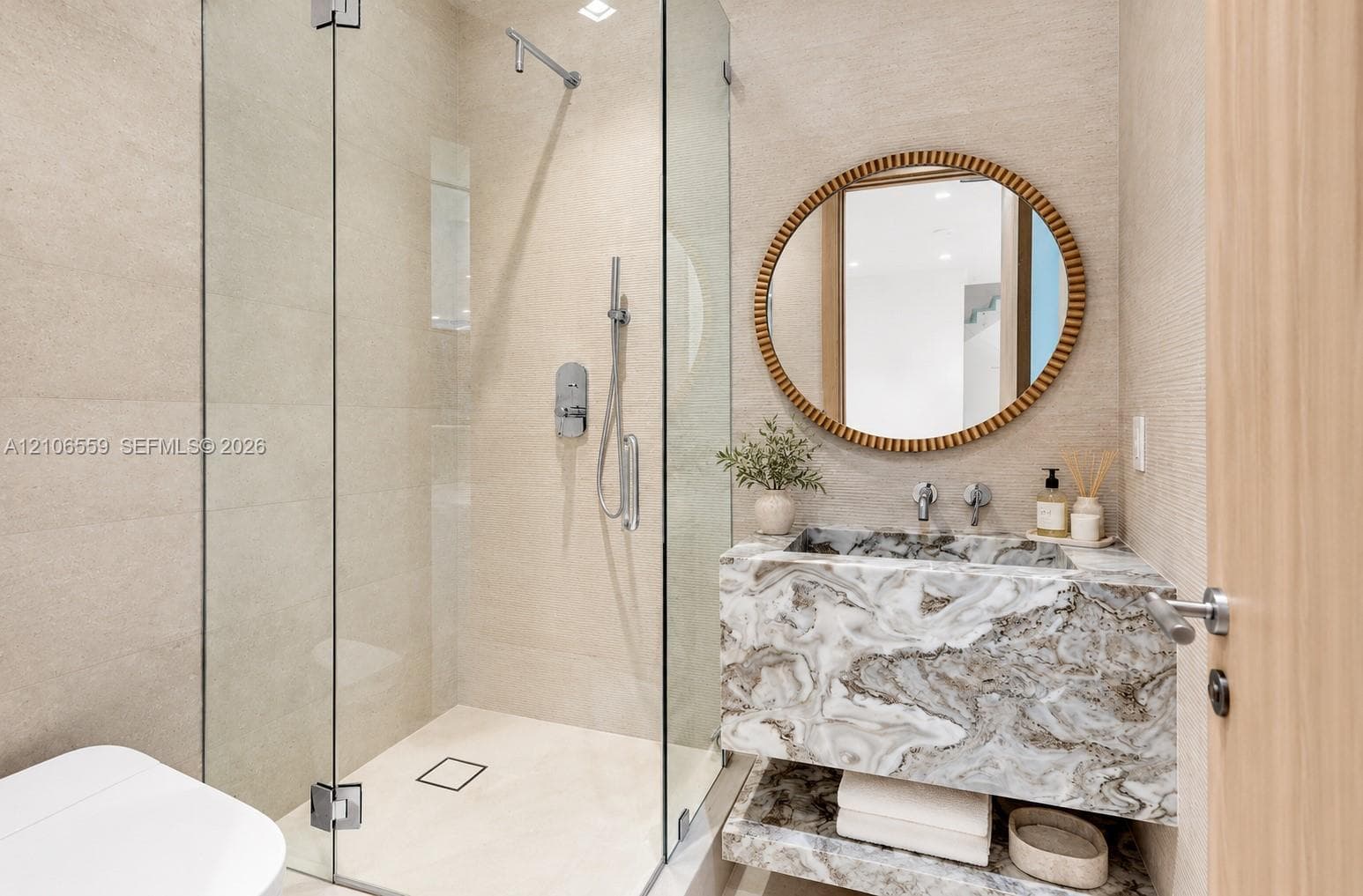 Glass-enclosed shower with wall-mounted plumbing fixtures, natural stone vanity with integrated basin, wall-mounted faucet, and textured wall finish