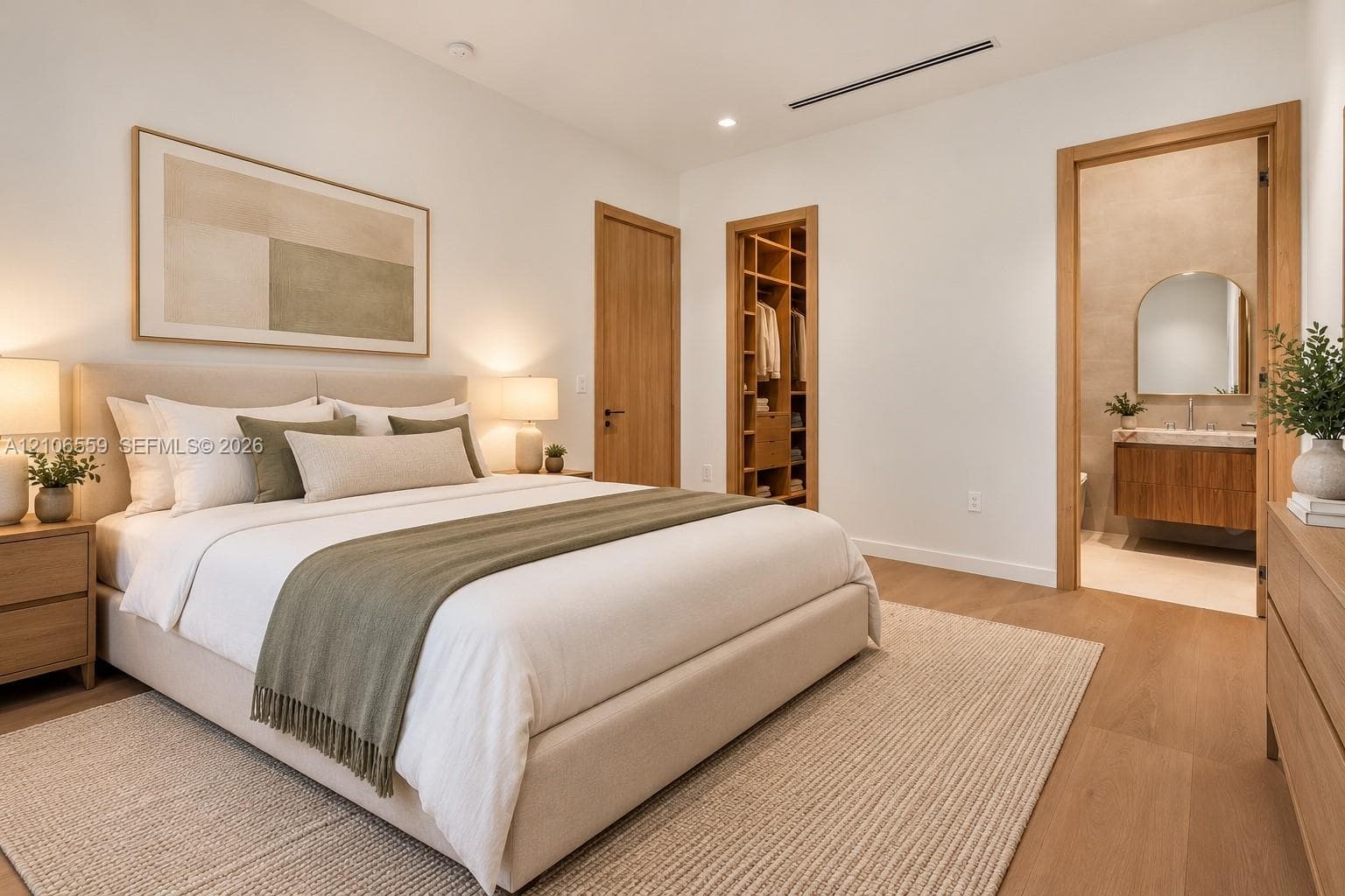 AI staged Bedroom featuring wood-finish flooring, recessed linear lighting, a custom built-in walk-in closet, and a bathroom entry with a floating vanity and arched mirror