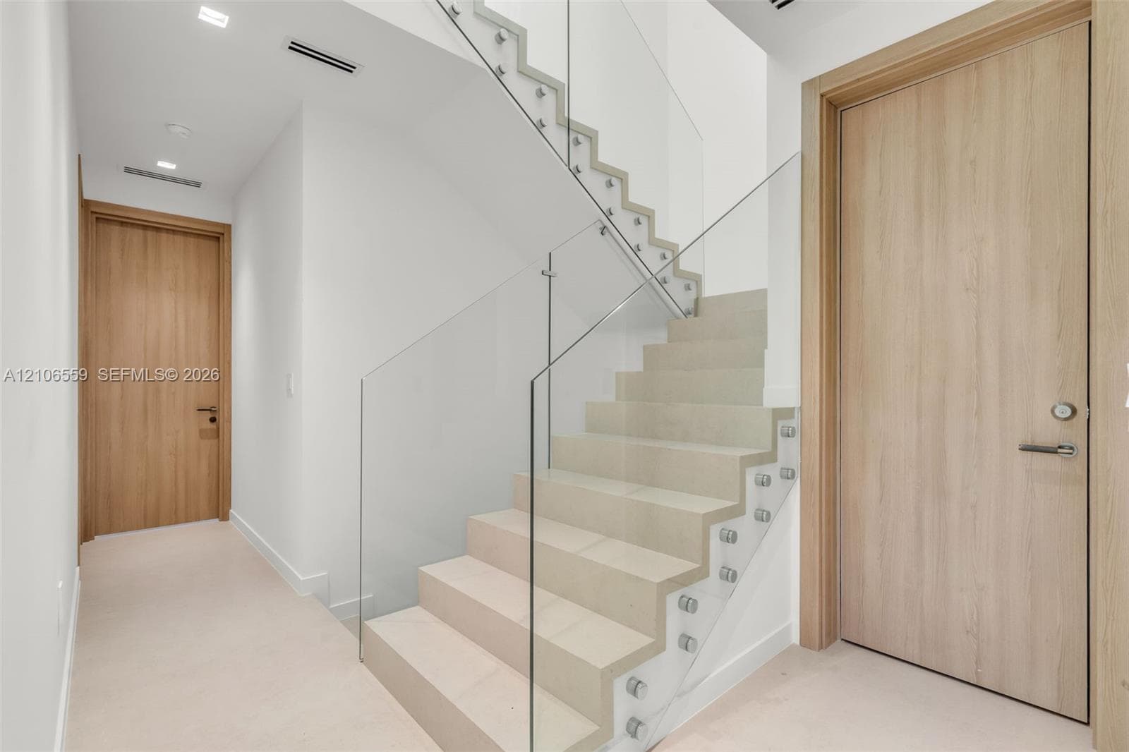 Staircase featuring stone treads, a frameless glass railing system, recessed ceiling lighting, and solid wood-finish interior doors