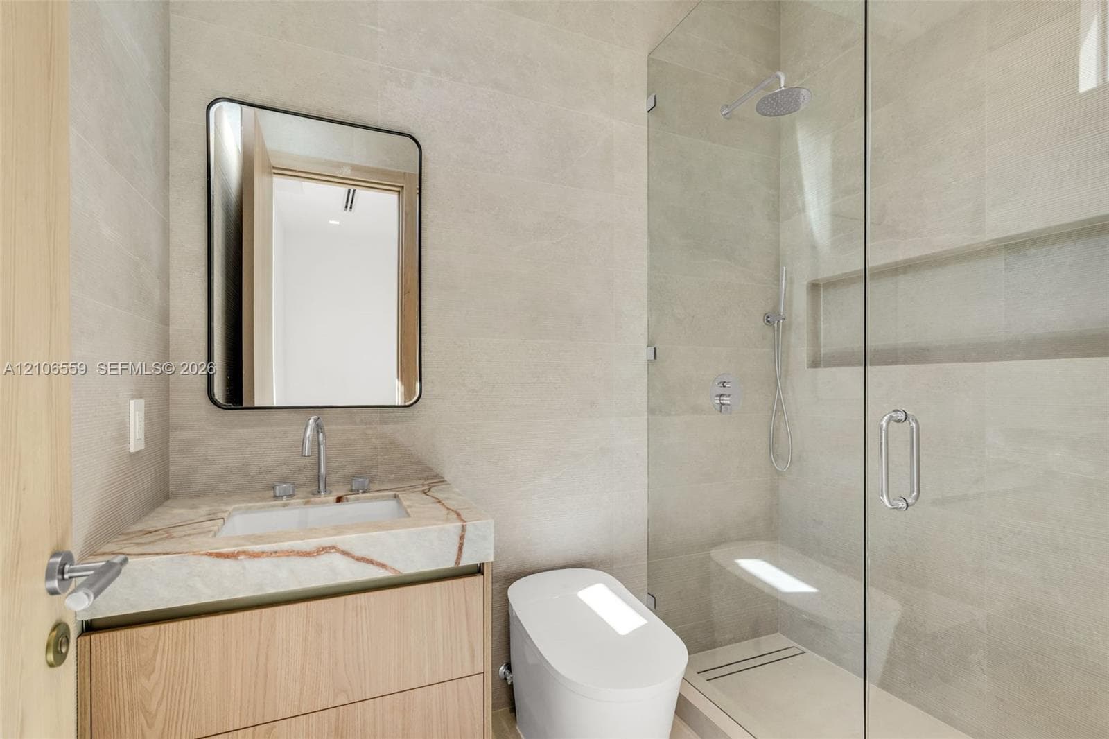 Floating wood-finish vanity with stone countertop, rectangular undermount sink, glass-enclosed shower featuring a built-in recessed niche, and wall-mounted mirror with rounded corners
