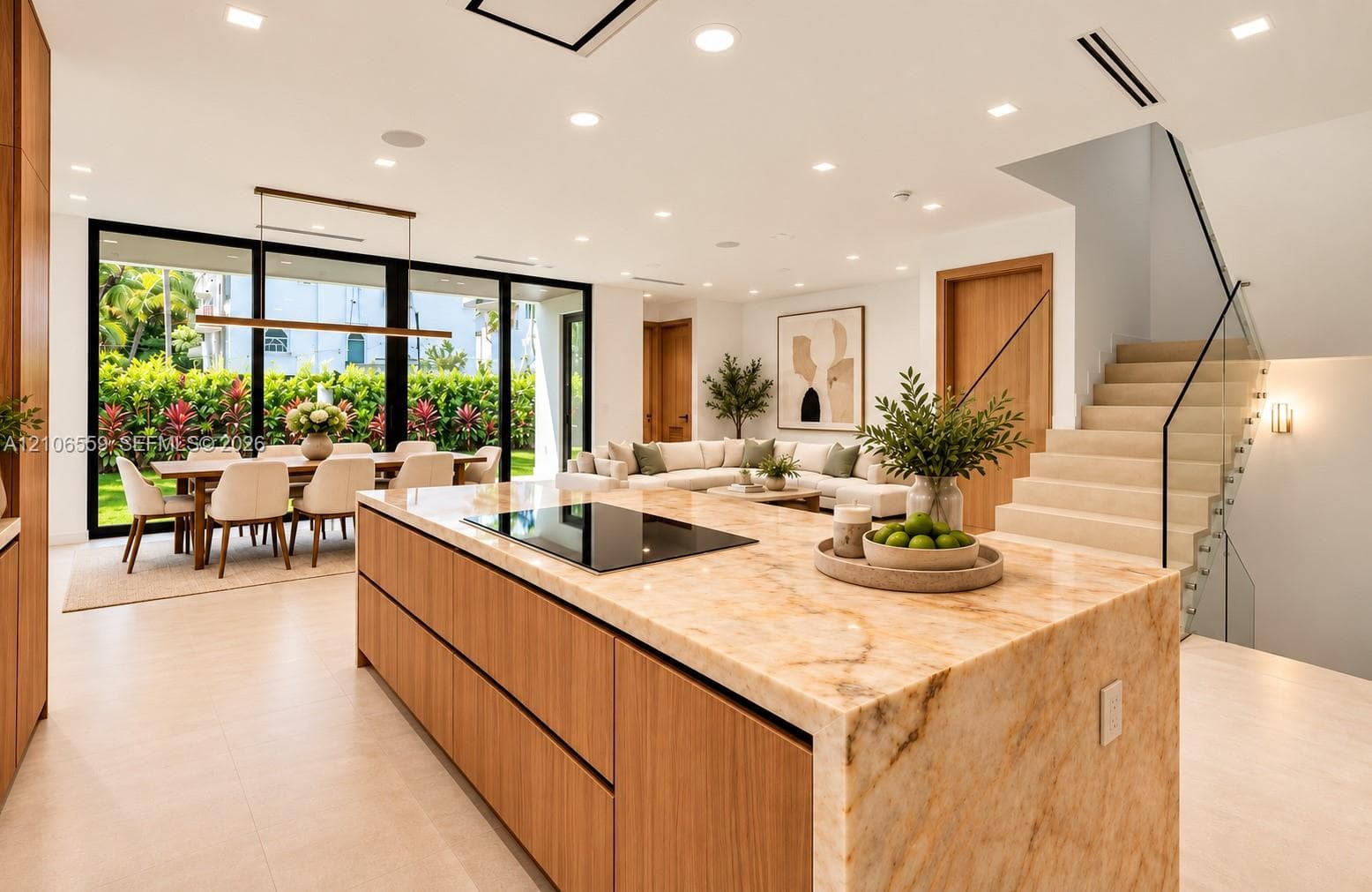 AI staged Kitchen island with waterfall stone countertop and integrated cooktop, wood-finish cabinetry, floor-to-ceiling glass sliding doors, staircase with glass railing, and recessed ceiling lighting