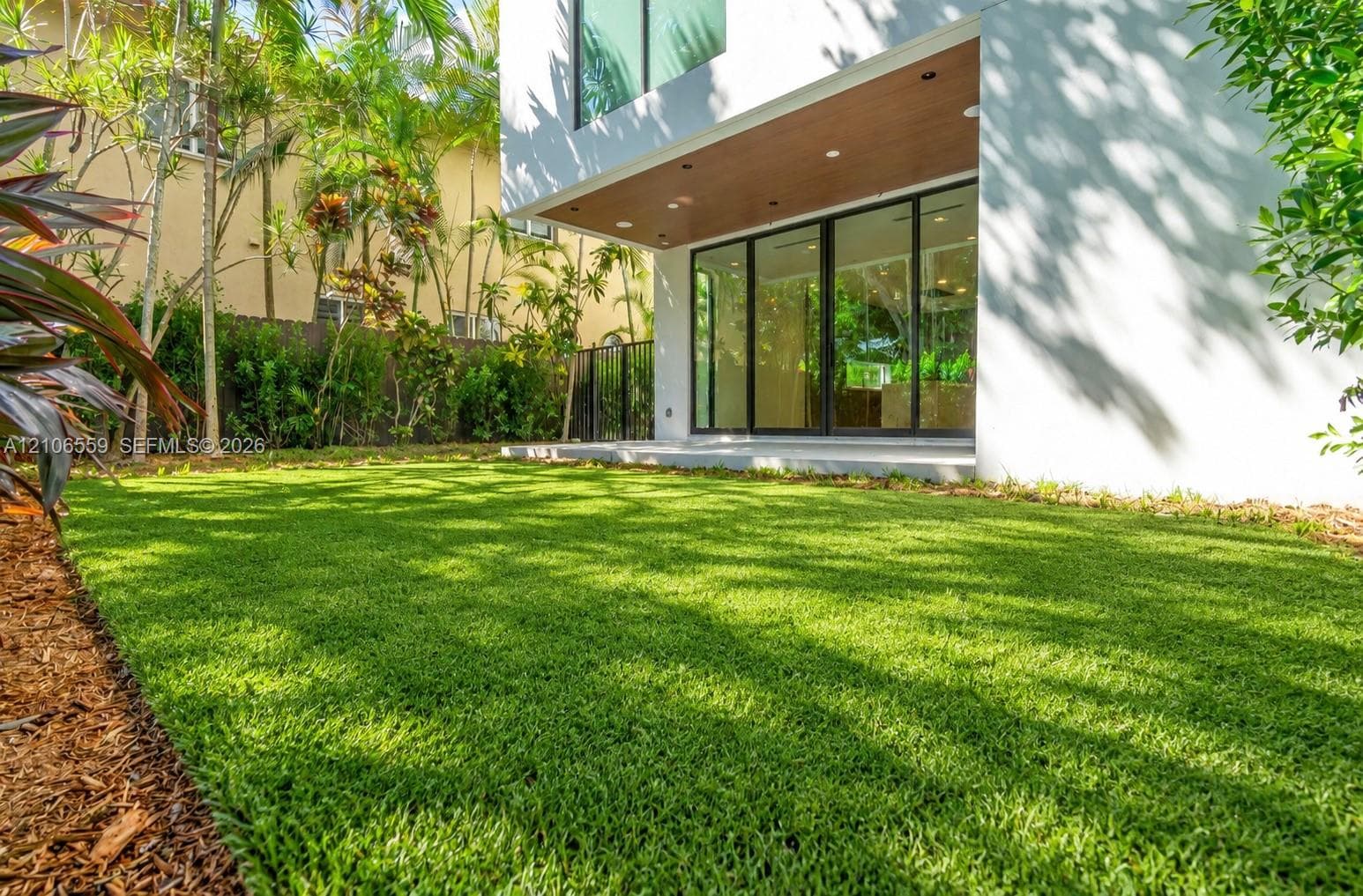 Backyard featuring synthetic turf, a covered patio with recessed lighting, multi-panel sliding glass doors, and mature landscaping