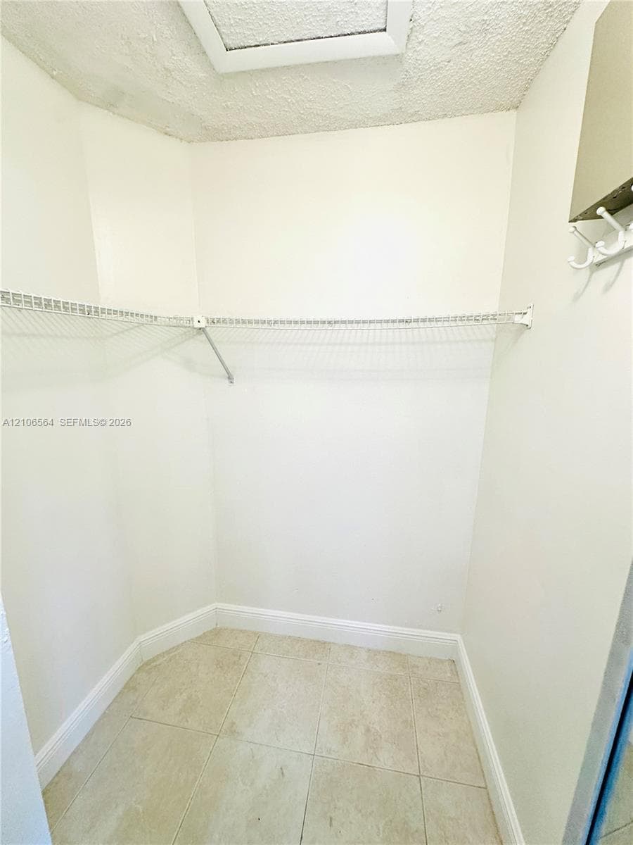 Storage space featuring white walls, light-toned tile flooring, built-in wire shelving, and a wall-mounted hook rack