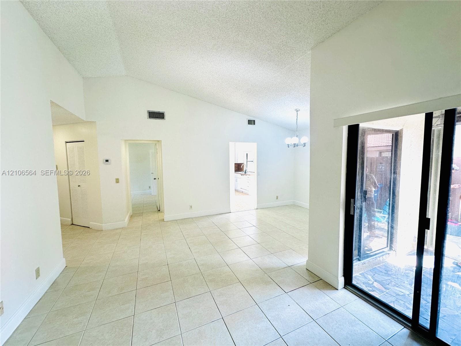 Vaulted ceilings, large-format neutral tile flooring, multi-pane sliding glass door, and overhead chandelier lighting
