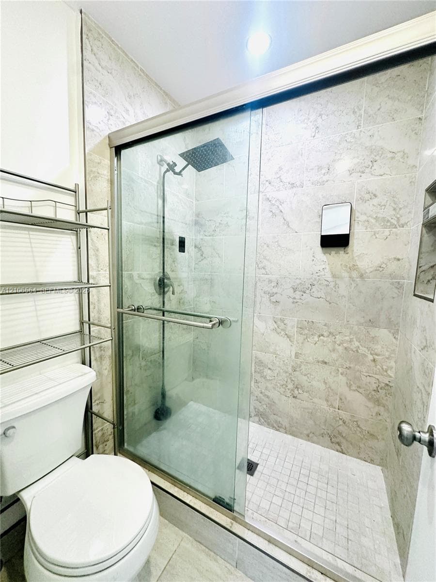 Shower enclosure featuring large-format tile wall surrounds, a rainfall showerhead, glass sliding doors, and a tiled shower floor
