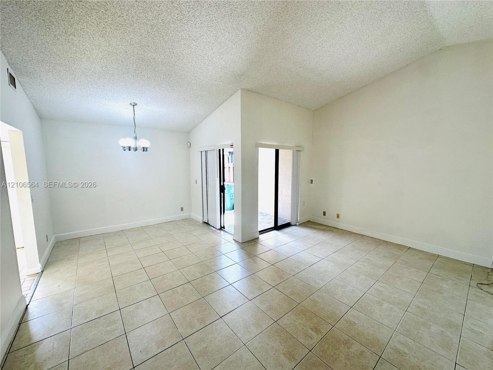 Vaulted ceilings, large-format tile flooring, dual sliding glass doors, and a multi-arm pendant light fixture