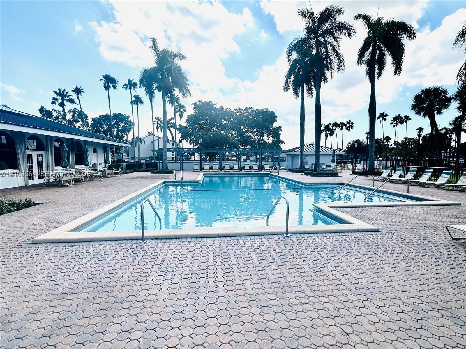 In-ground swimming pool with metal handrails, surrounded by extensive stone paver decking and mature palm trees