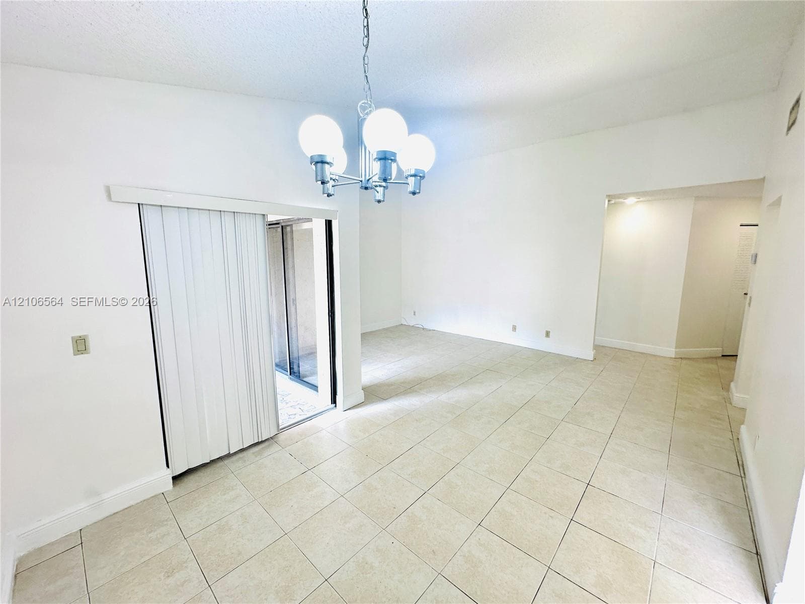 High-ceilinged interior featuring ceramic tile flooring, a multi-globe chandelier, and sliding glass doors with vertical blinds