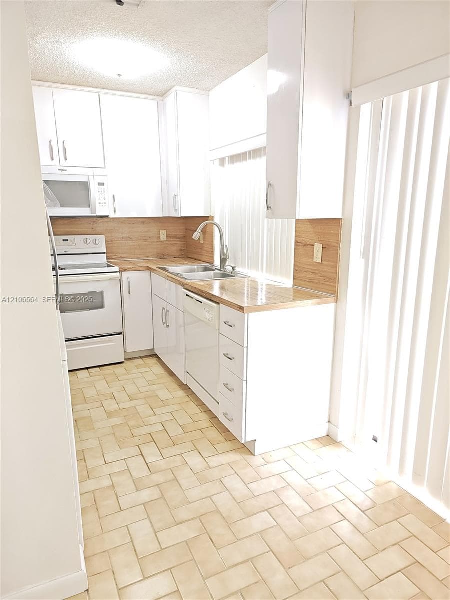 Kitchen featuring white cabinetry, wood-finish countertops, stainless steel sink with a high-arch faucet, white built-in appliances, and herringbone-patterned tile flooring