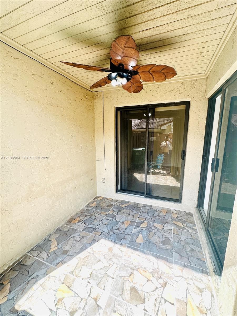 Covered patio featuring multi-tonal stone-tile flooring, beadboard ceiling, and a decorative leaf-blade ceiling fan with integrated lighting