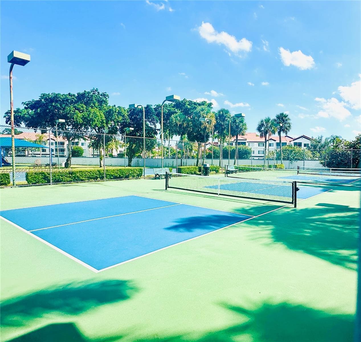 Multi-court pickleball facility featuring high-visibility blue and green court surfaces, chain-link perimeter fencing, pole-mounted lighting, and integrated seating areas