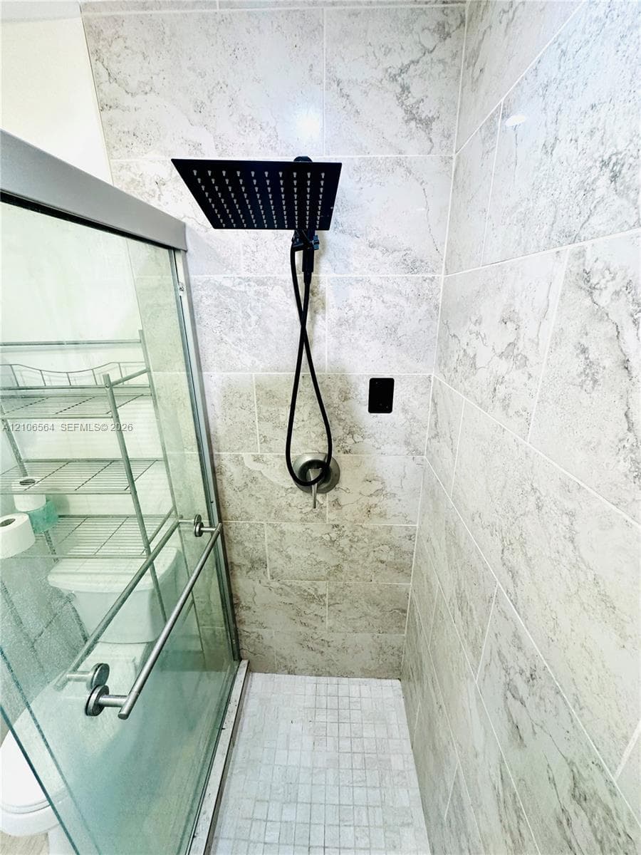 Walk-in shower enclosure featuring large-format stone-patterned wall tile, square rainfall showerhead, integrated handheld sprayer, and mosaic tile flooring