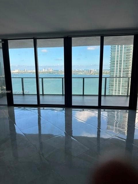 Floor-to-ceiling glass windows, high-gloss tile flooring, and a glass-paneled balcony overlooking the water and urban skyline