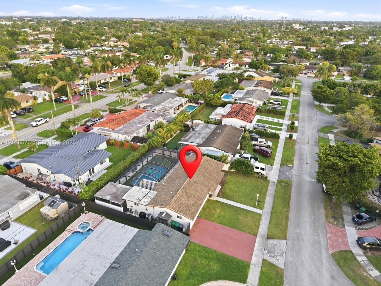 Aerial perspective featuring a screened-in swimming pool, a composition shingle roof, and a paved driveway