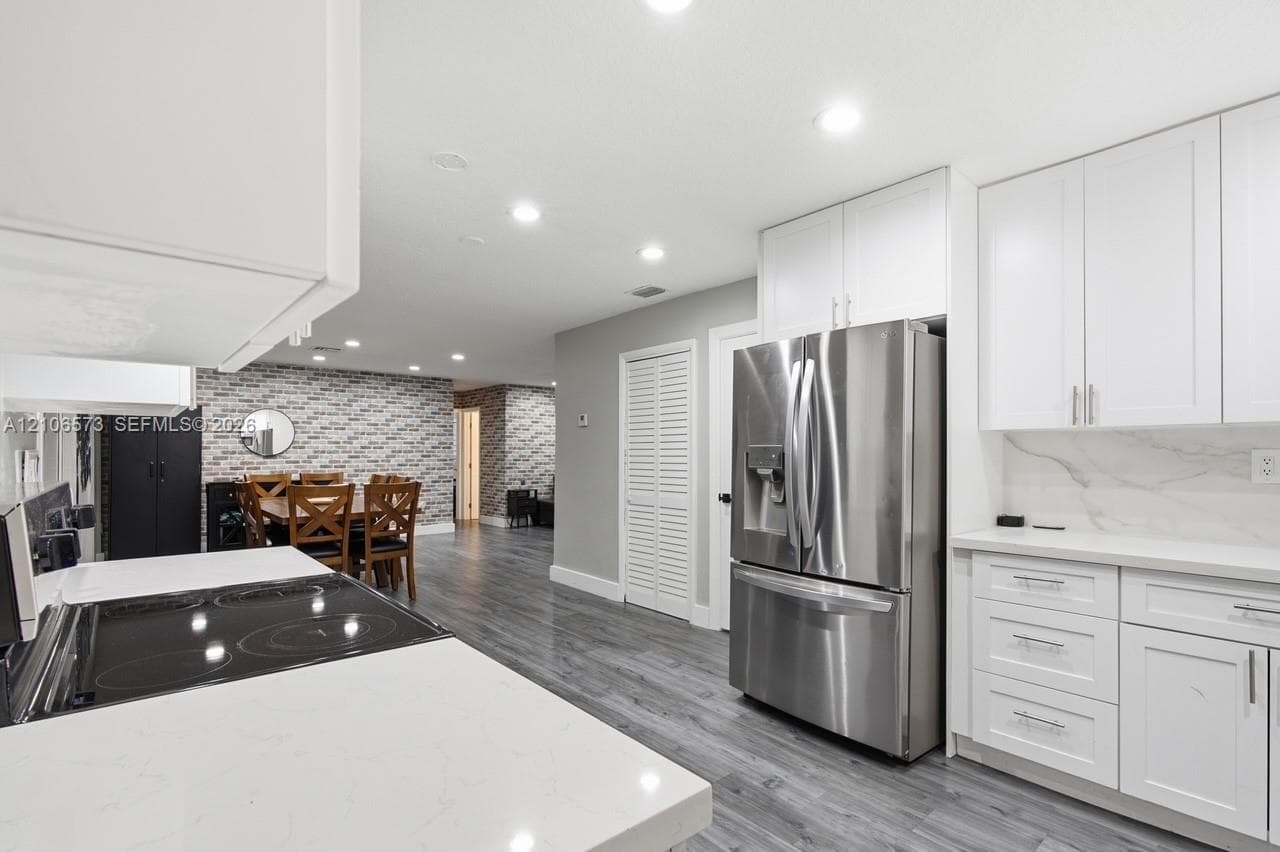 Kitchen featuring white cabinetry, solid-surface countertops, stone-patterned backsplash, stainless steel refrigerator, and wood-finish flooring