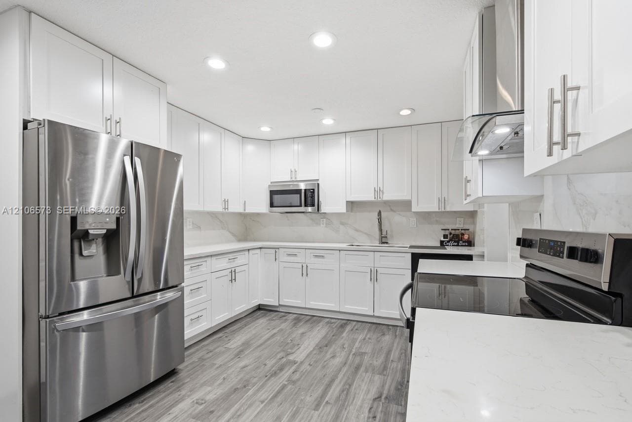 Kitchen featuring white shaker-style cabinetry, stainless steel appliances, stone-finish countertops, full-height backsplash, and wood-finish flooring