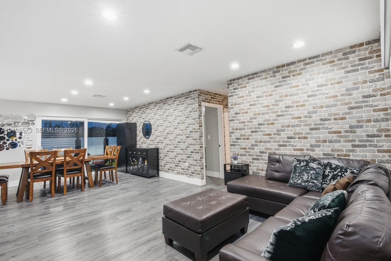 Interior space featuring full-height textured brick accent walls, wood-finish flooring, recessed lighting, and a sliding glass door