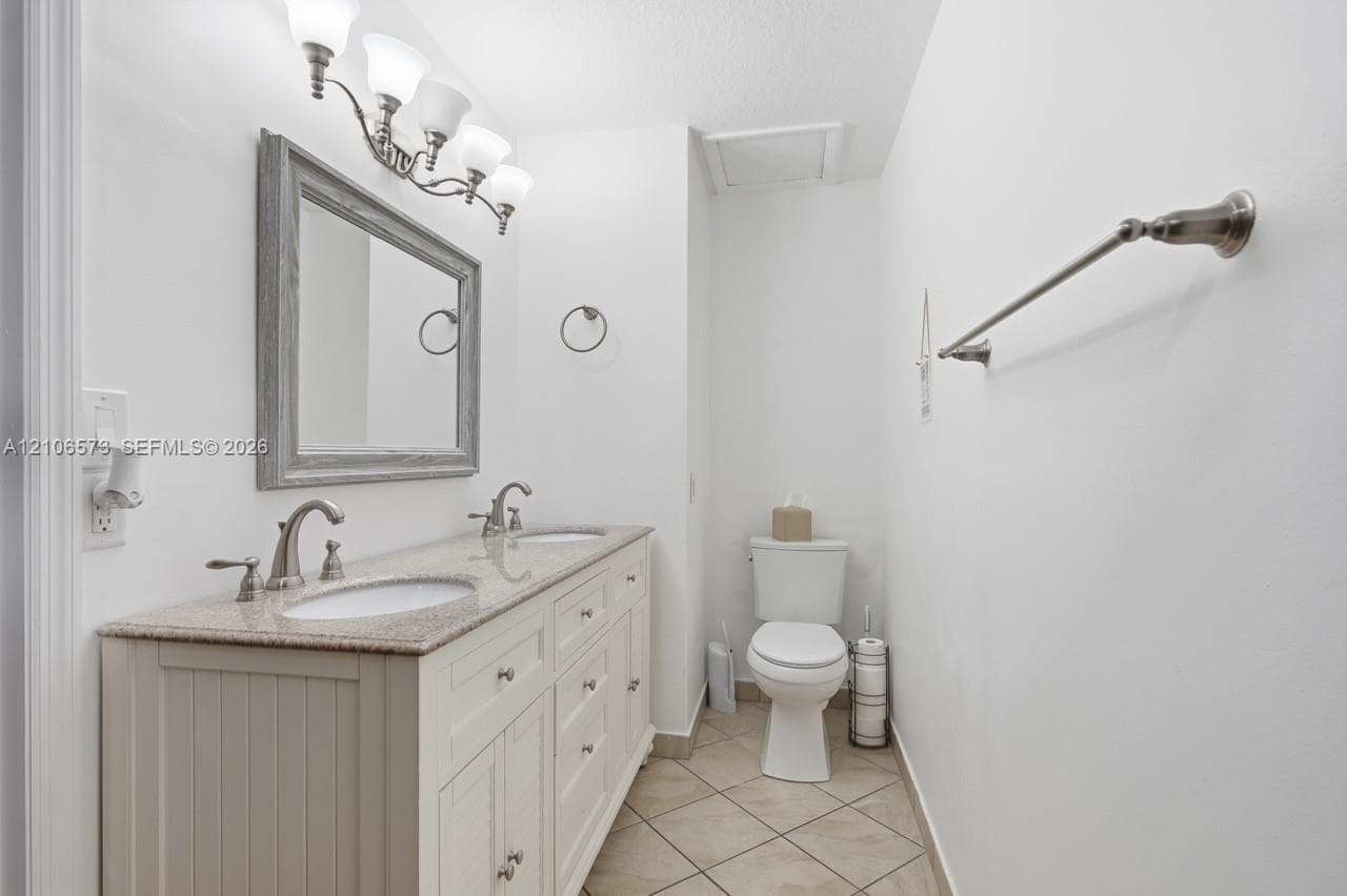 Double vanity featuring a stone countertop, dual undermount sinks, shiplap-style cabinetry, a framed mirror, and brushed-nickel lighting and fixtures