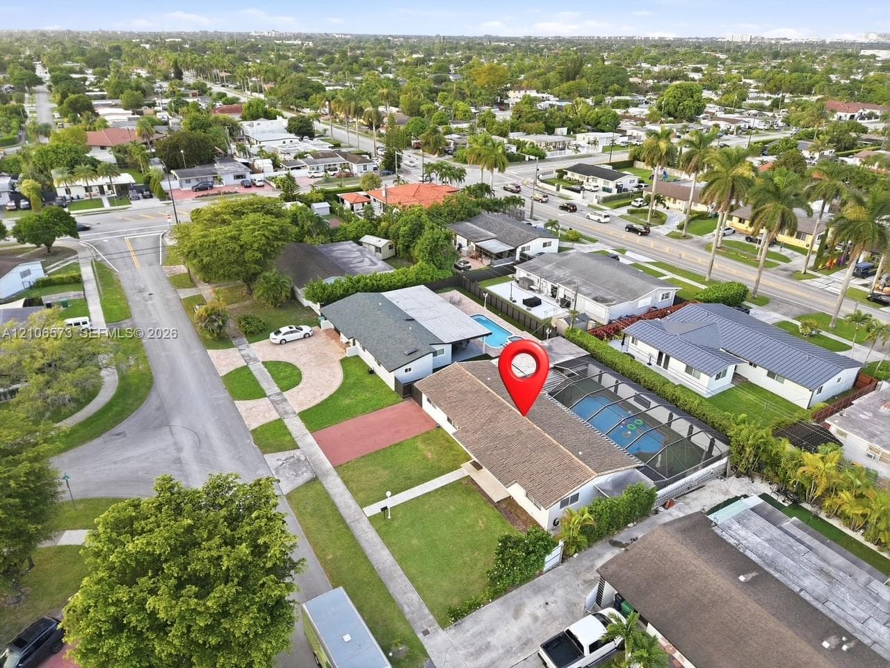 Aerial perspective of a single-story residence featuring a shingle roof, a screened-in swimming pool, a front lawn, and a paved driveway